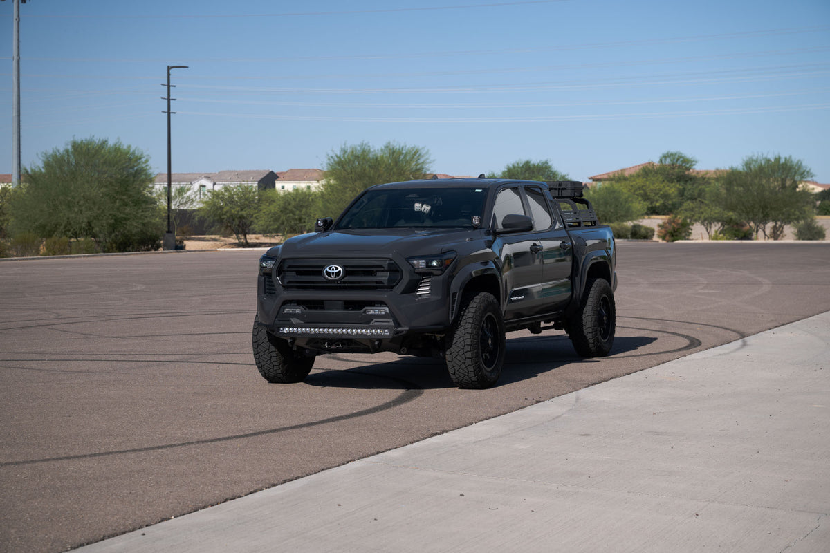Black Toyota Tacoma with Stealth Fighter Winch Front Bumper on a paved road with trees and houses in the background