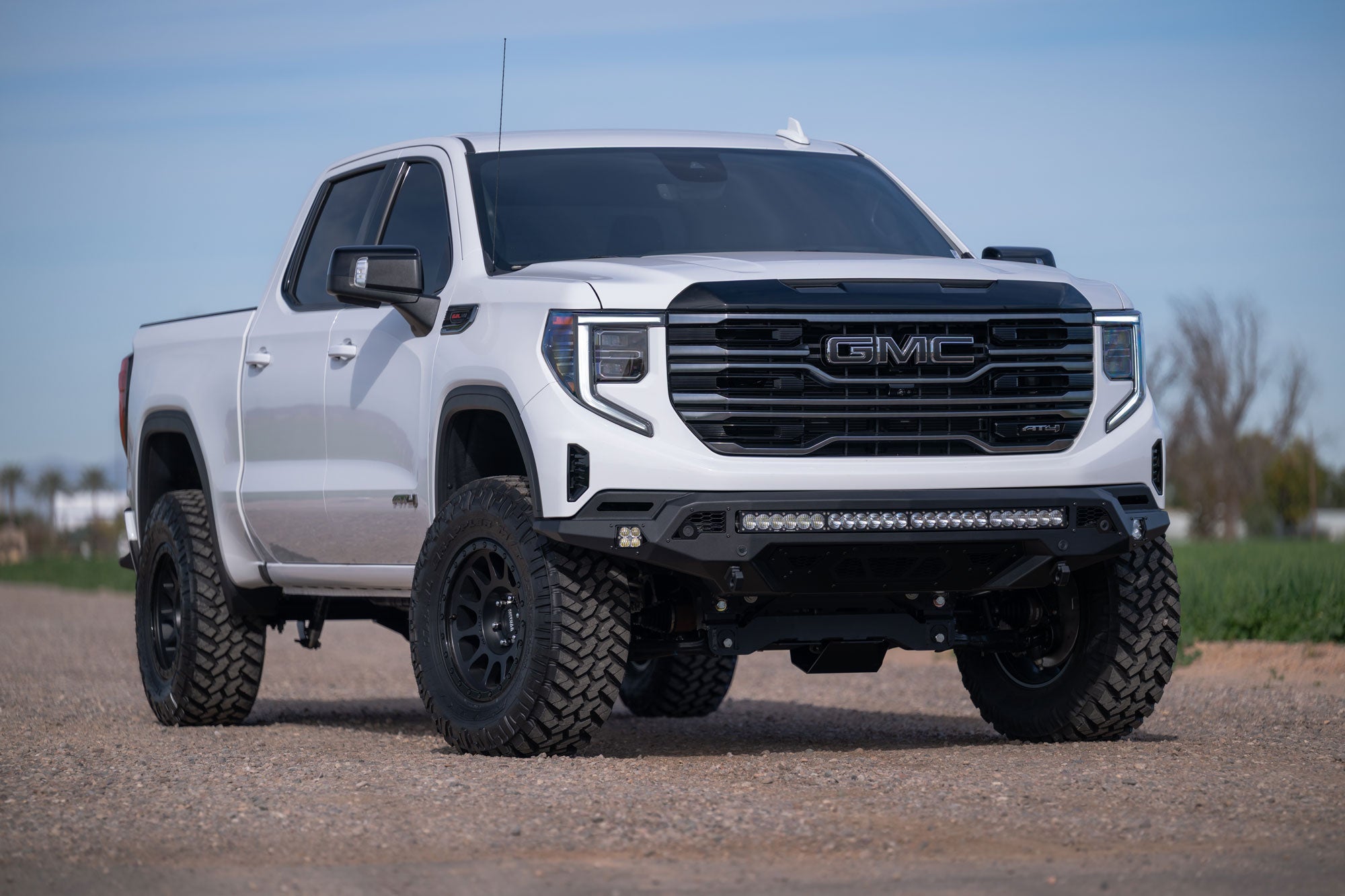 White GMC Sierra 1500 with Stealth Fighter Front Bumper on a road with a clear sky background
