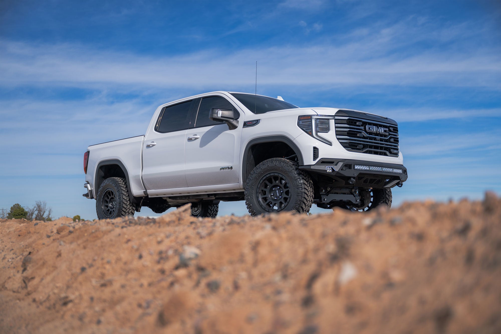 White GMC Sierra 1500 with Stealth Fighter Front Bumper on a dirt road with a blue sky background