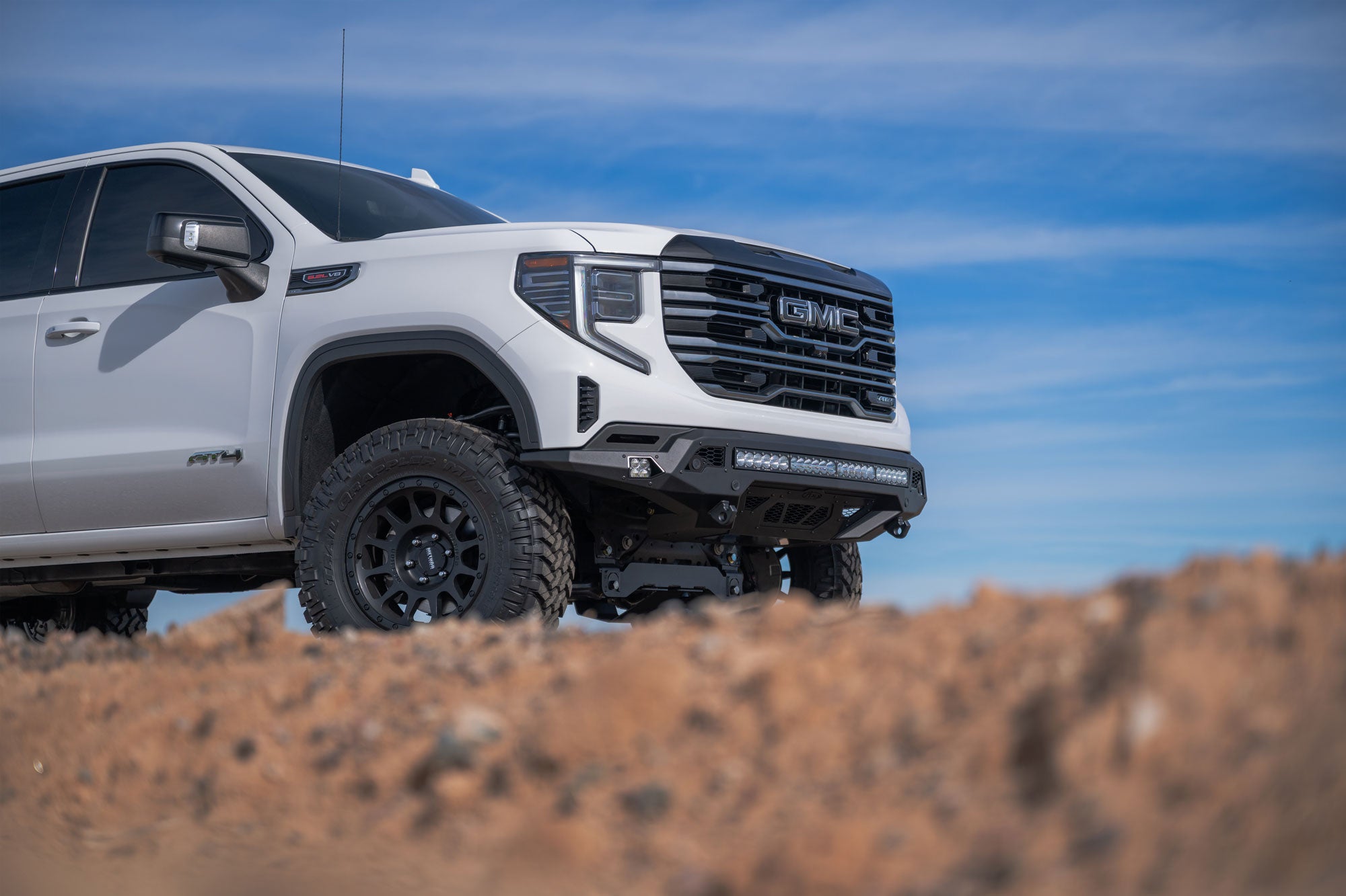 White GMC Sierra 1500 with Stealth Fighter Front Bumper on a dirt road with a clear blue sky