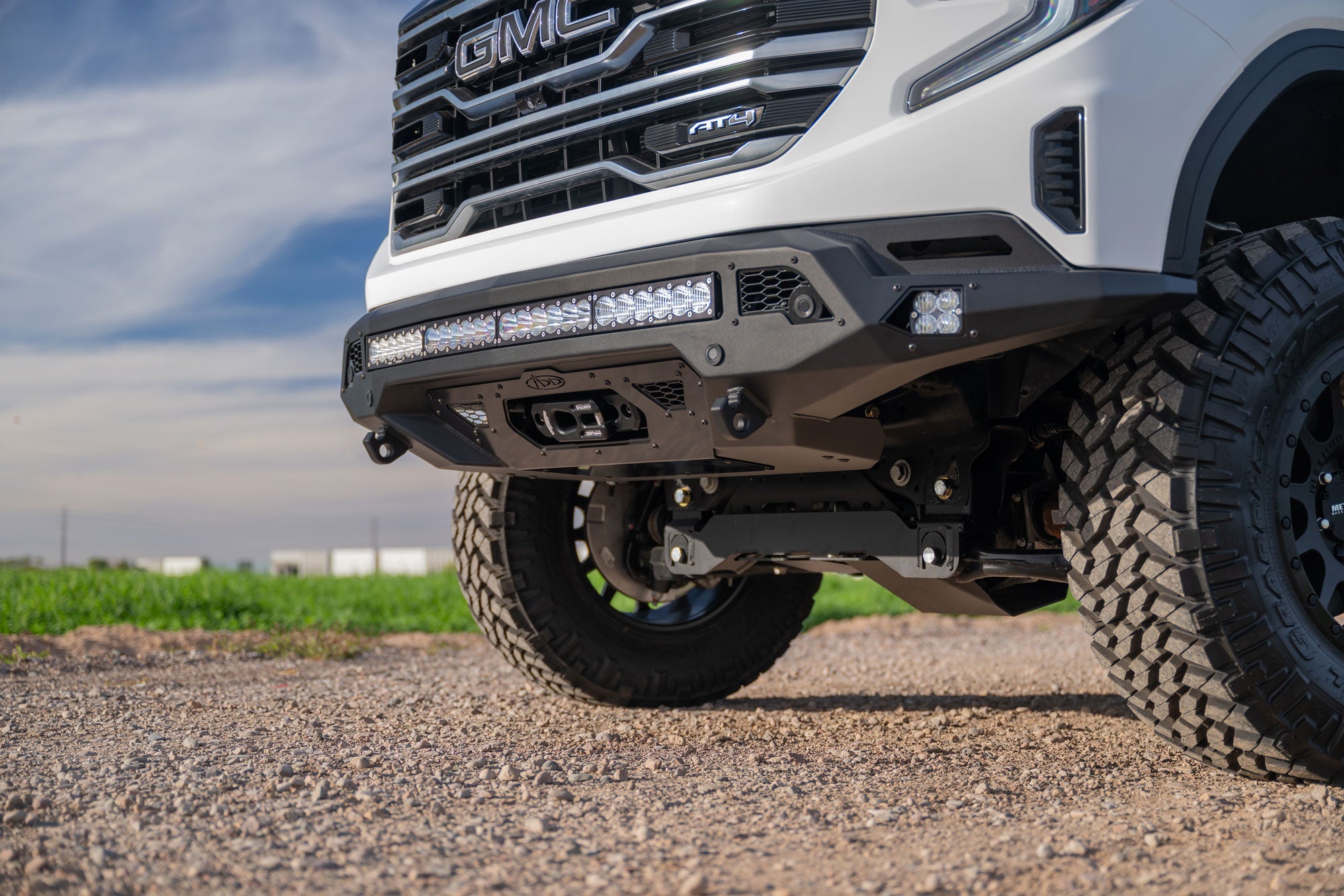 Close-up of a GMC Sierra 1500 with Stealth Fighter Front Bumper and Winch Kit Upgrade on a gravel road.