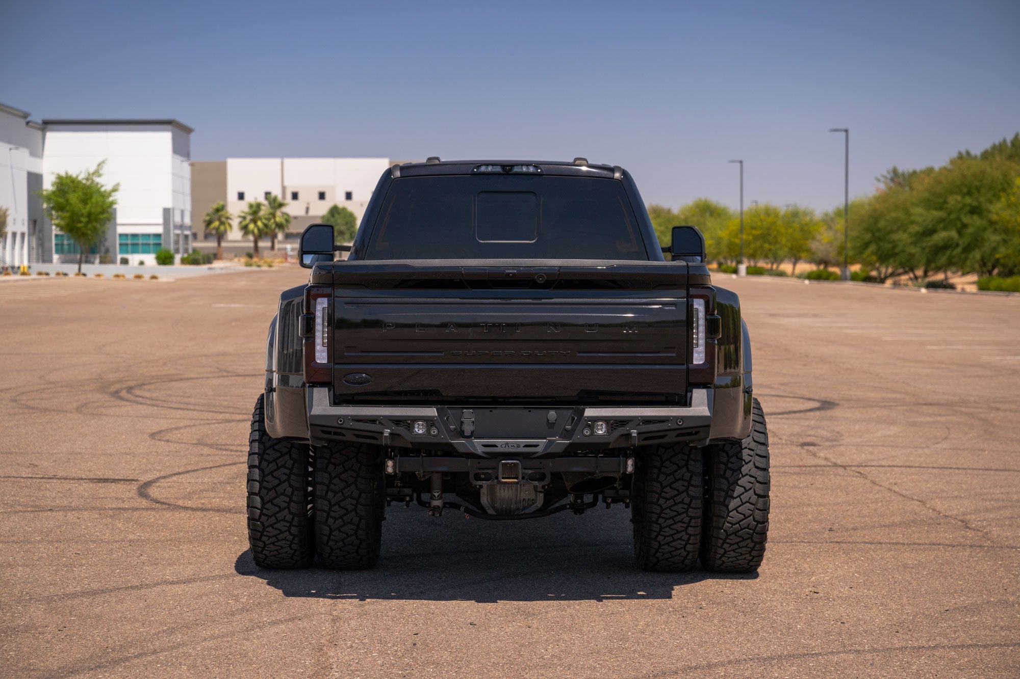 Back view of Stealth Fighter Rear Bumper for 2023-2026 Ford Super Duty in an open parking lot with buildings and trees in the background.