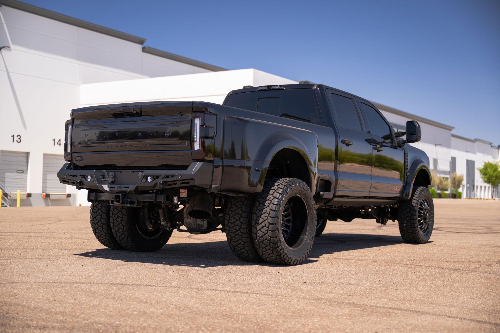 Black 2023-2026 Ford Super Duty with Stealth Fighter Rear Bumper parked in front of a building with a clear blue sky.