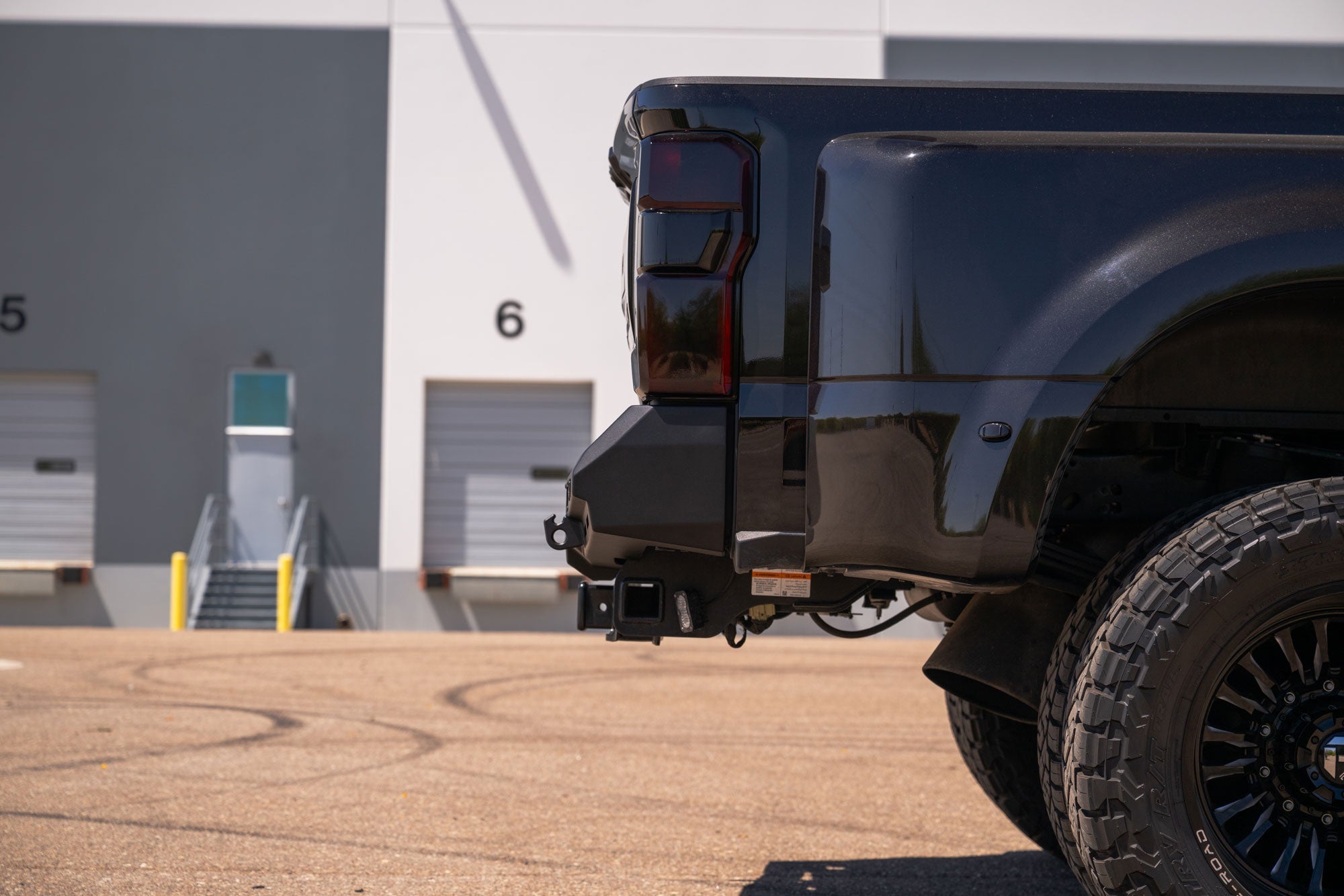 Stealth Fighter Rear Bumper for 2023-2026 Ford Super Duty, side profile view, parked in front of a warehouse.