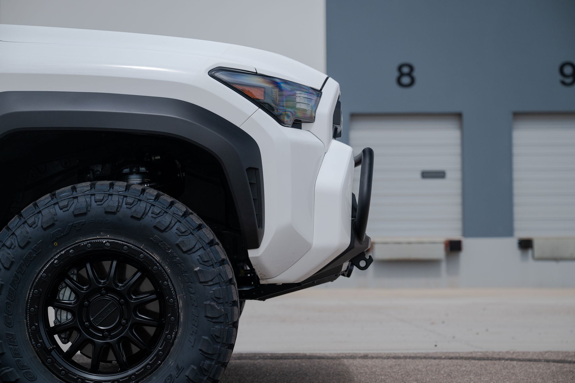 Close-up of a 2025 Toyota 4Runner Stealth Center Mount Front Bumper with Top Hoop in front of a building with garage doors.