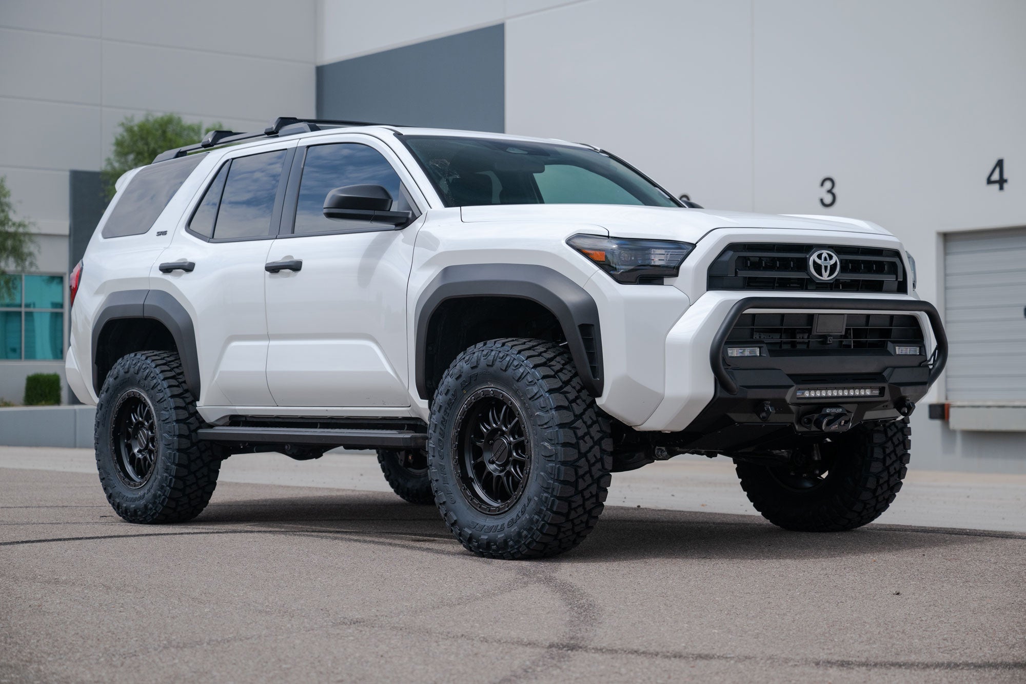 2025 Toyota 4Runner Stealth Center Mount Front Bumper with Top Hoop with lifted tires and off-road accessories in front of a building.