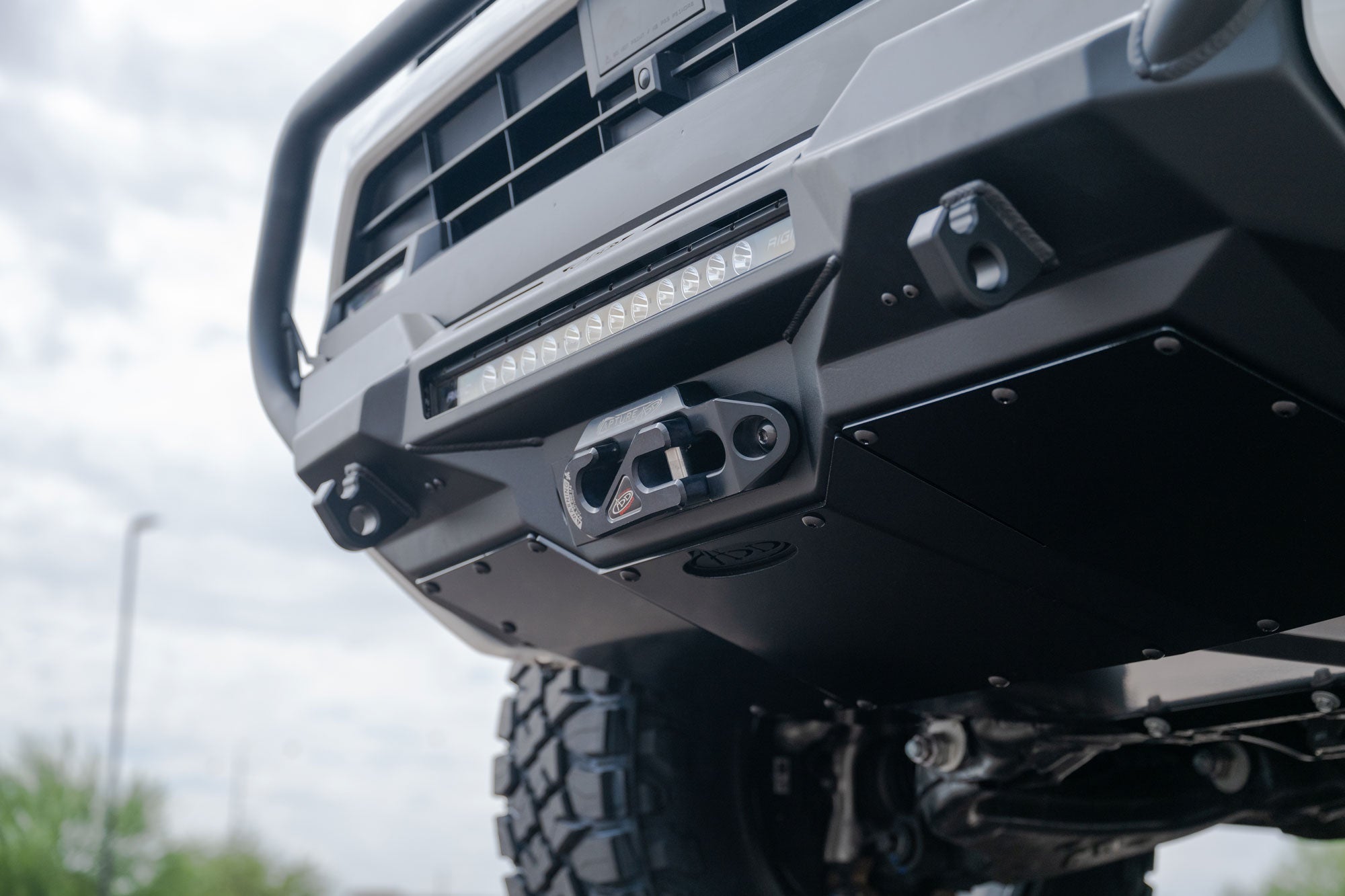 Close-up of a 2025 Toyota 4Runner Stealth Center Mount Front Bumper with Top Hoop with off-road lights against a cloudy sky.