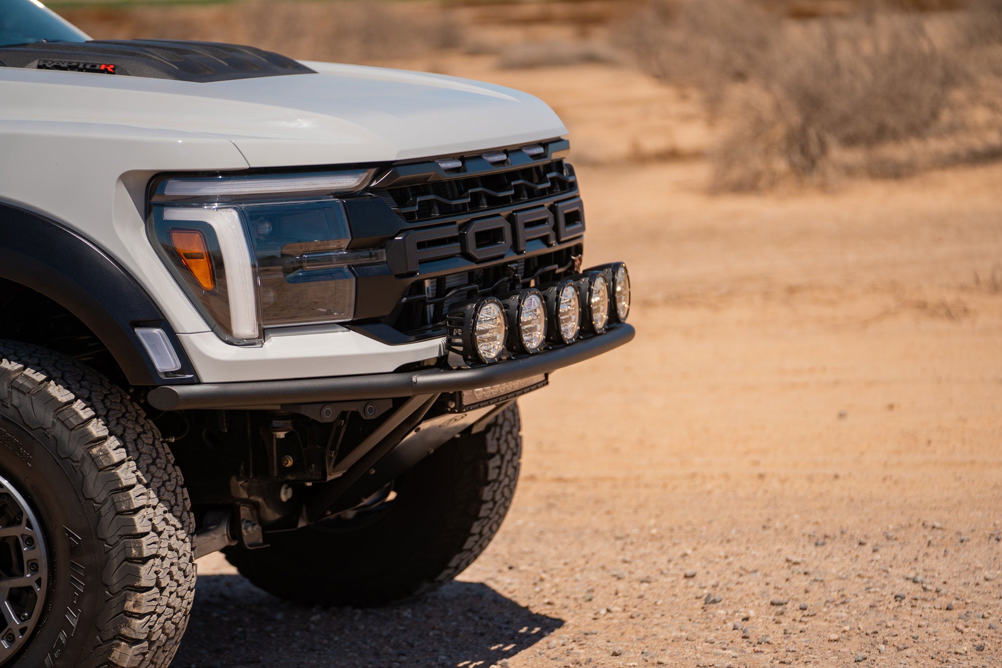 Angled view of the 2021+ Ford F-150 Raptor Pro Plus Frame Cut Front Bumper installed on white Ford Raptor truck with maximum lighting