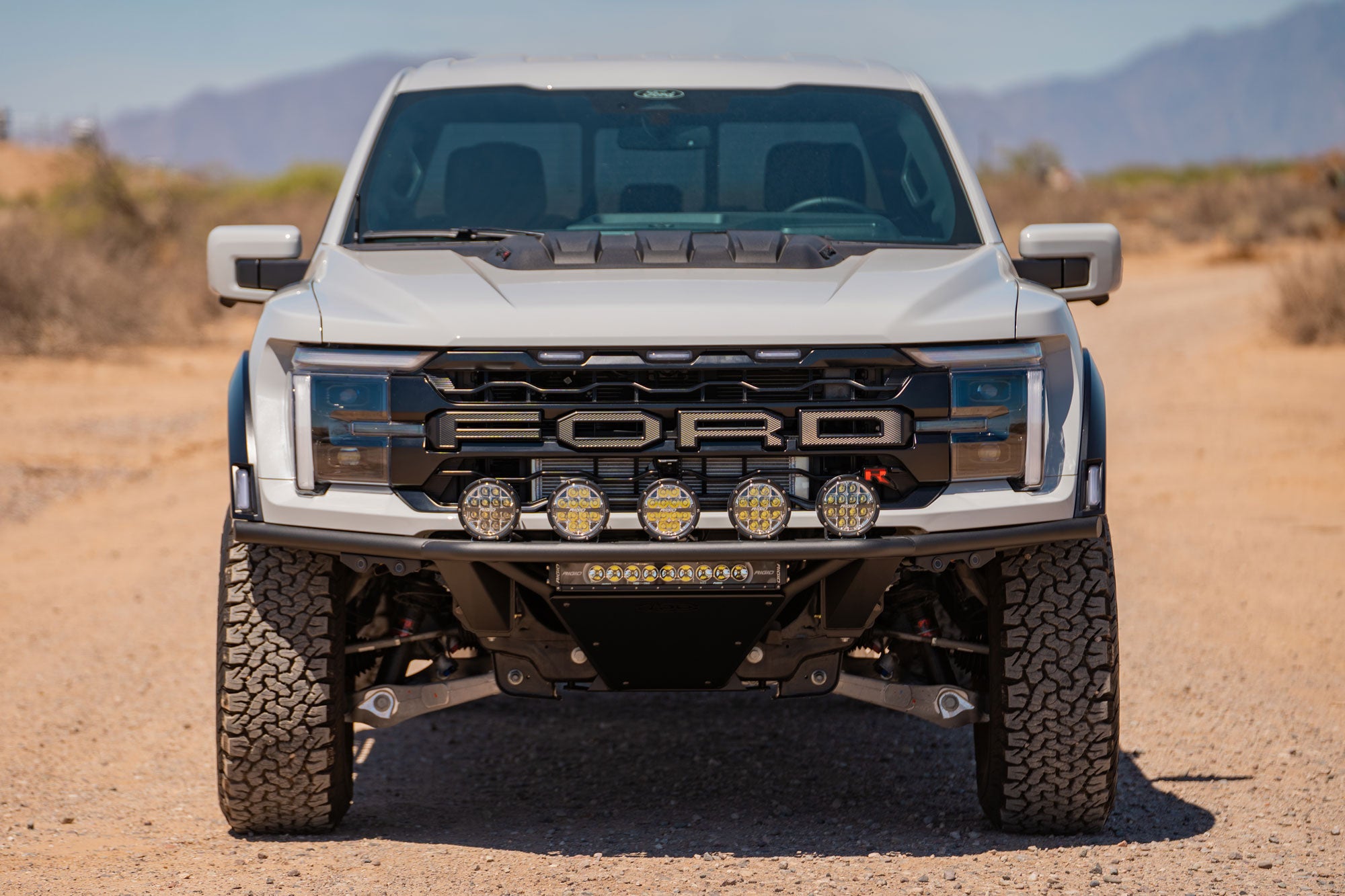Front view of 2021+ Ford F-150 Raptor Pro Plus Frame Cut Front Bumper installed on white Ford Raptor in the desert mountains